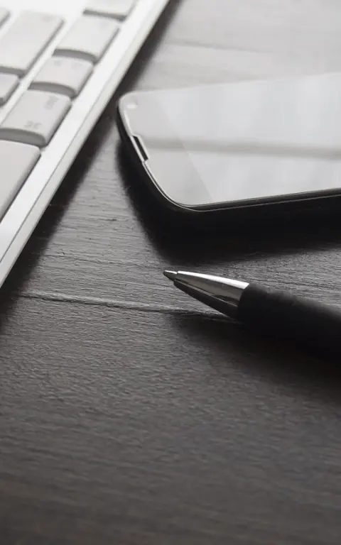 Trois moyens de contact. Un stylo à bille noir avec une pointe de couleur acier est posé à côté d'un clavier d'ordinateur et d'un smartphone. Le clavier est placé sur la gauche, le mobile en haut à droite et le stylo sous le mobile. Le stylo pointe vers le clavier.