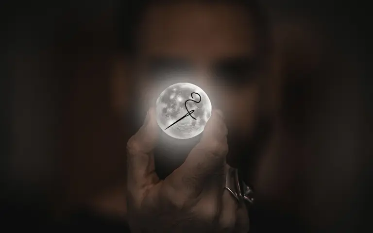 Une main tient la lune illuminée entre l'index et le majeur. Une aiguille avec du fil est appliquée sur l'astre. Ceci représente l'univers broderie d'Au Bijou Brodé.